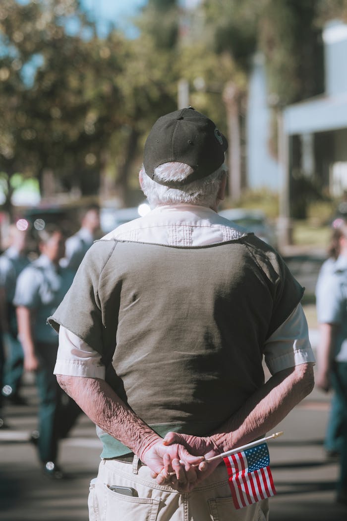 Senior man watching a parade holding a small American flag outdoors.